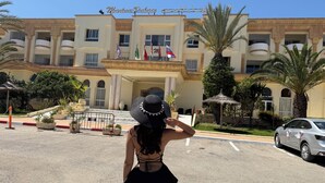 A hotel entrance with a grand facade, multiple balconies, and flags.