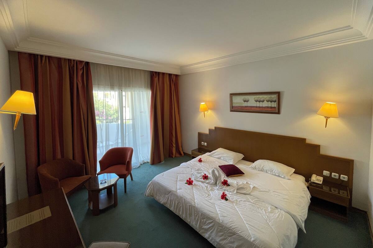 Ein Hotelzimmer mit einem Bett, zwei Stühlen, einem Tisch, einer Lampe und einem Bild an der Wand.
