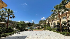 A courtyard with a marble floor, palm trees, and a pool area.