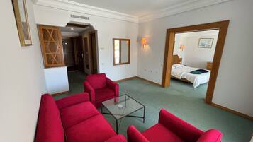 Una habitación de hotel con un sofá rojo, una mesa de centro de vidrio, una cama con ropa de cama blanca y un espejo con marco de madera.
