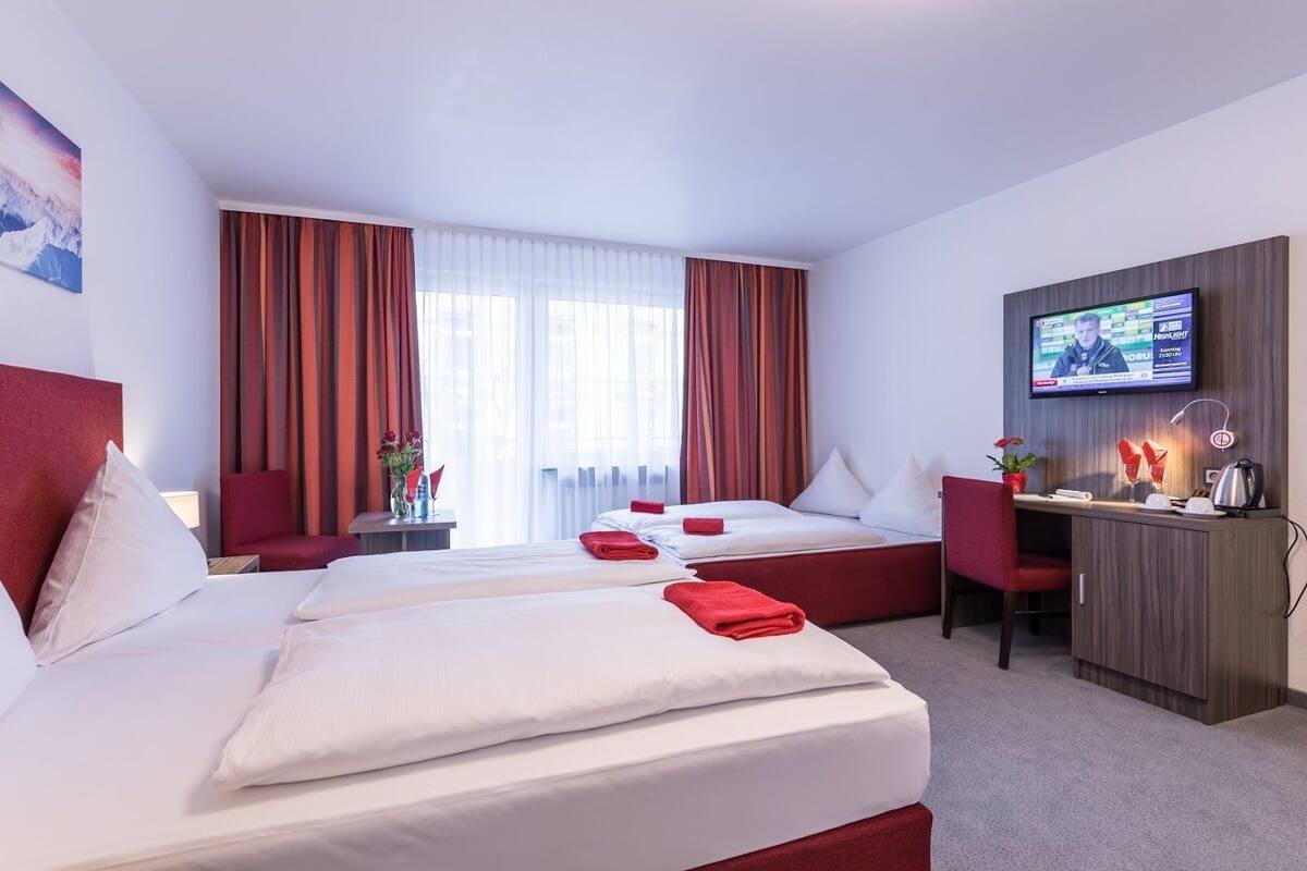 A hotel room with two beds, a desk, a TV, and a window with curtains.