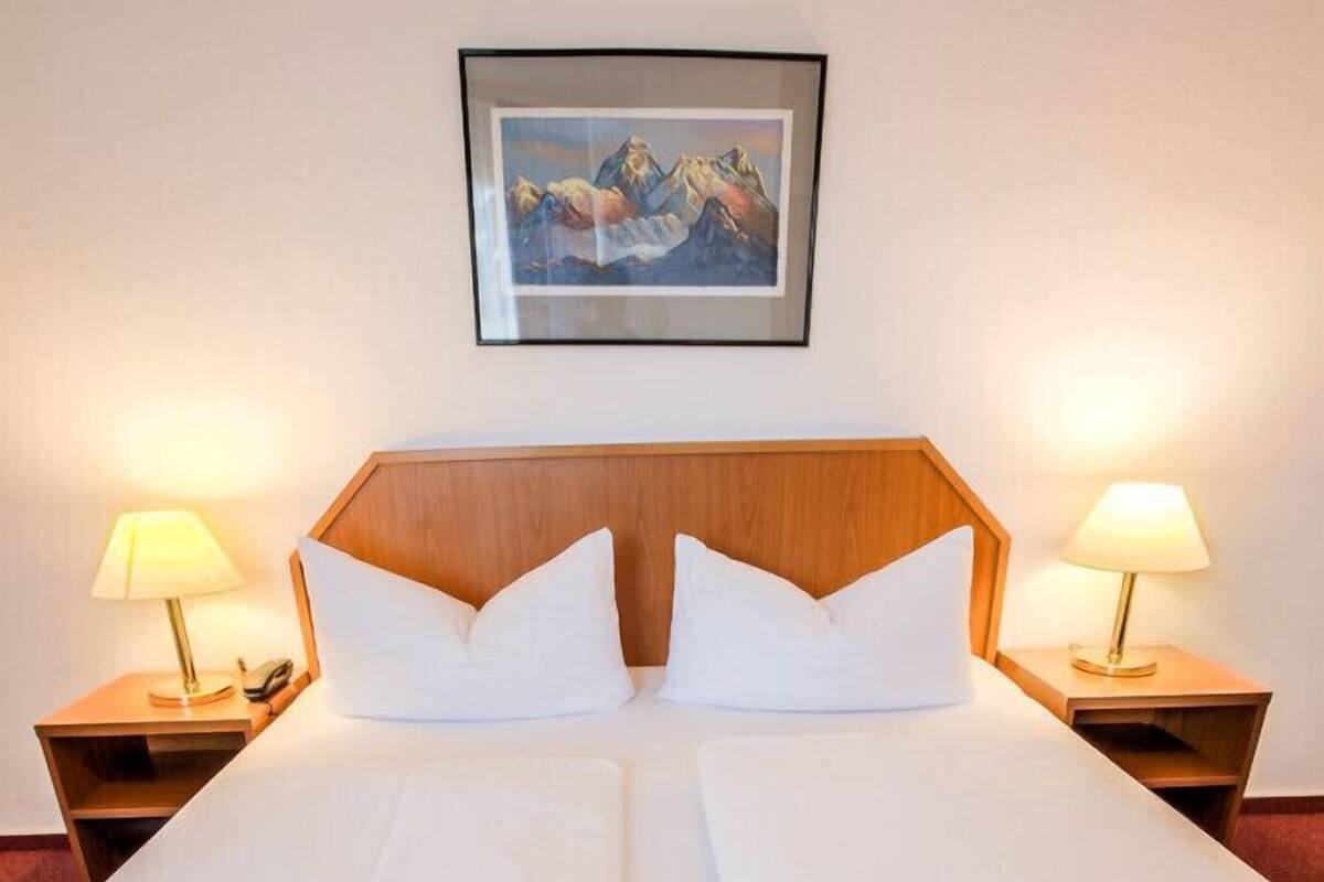 A double bed with white linens, two bedside tables with lamps, and a framed picture on the wall.