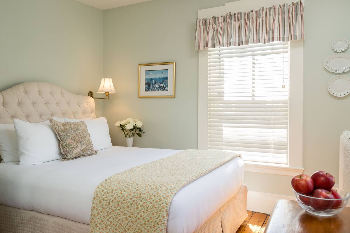 A neatly made bed with a floral bedspread, a bedside lamp, and a framed picture on the wall.