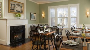 A dining area with wooden tables, black chairs, a fireplace, and framed artwork on the walls. - Brass Lantern Inn (Nantucket)