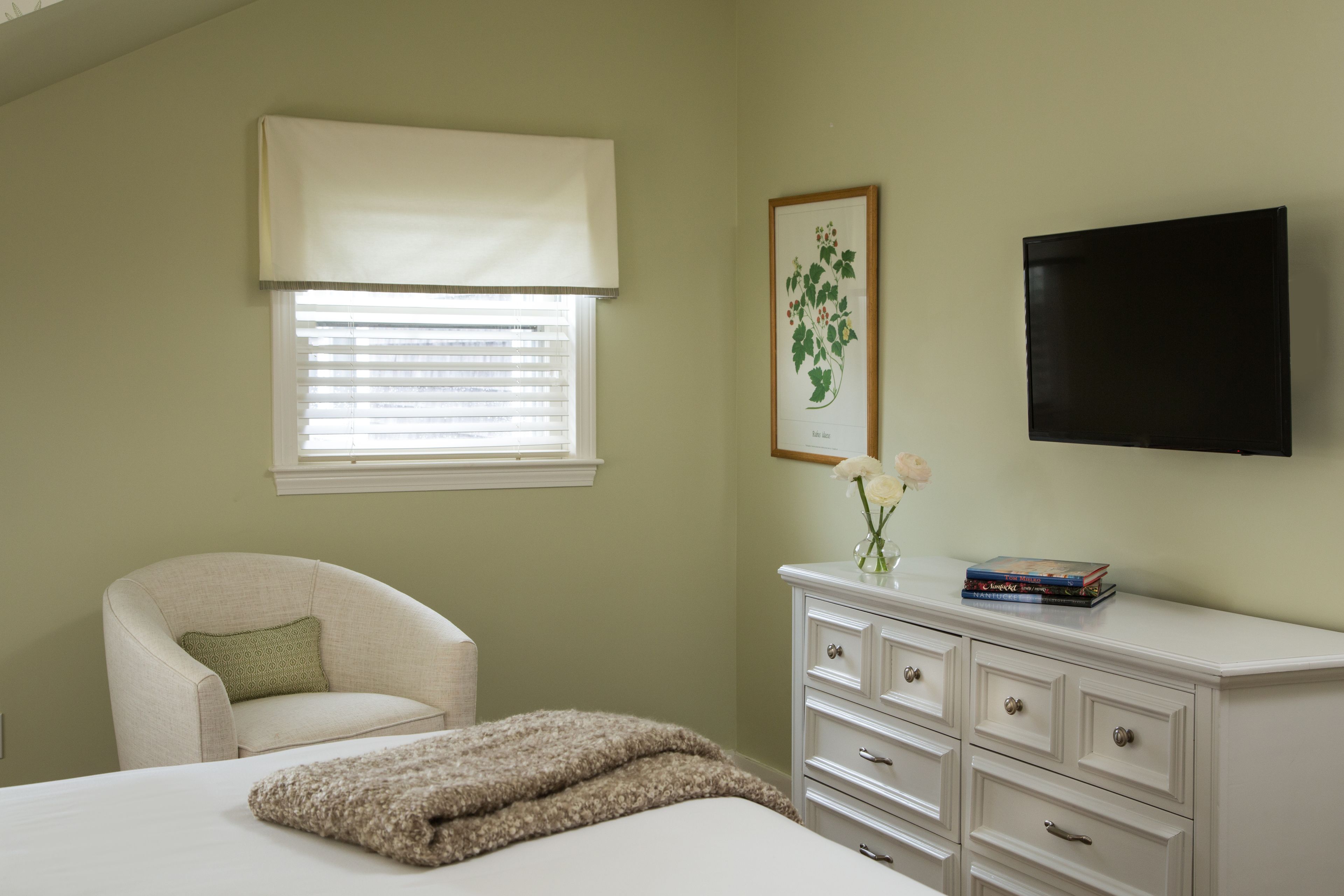 A bedroom with a bed, a chair, a dresser, a television, and a window with blinds.