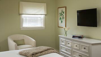 A bedroom with a bed, a chair, a dresser, a television, and a window with blinds.