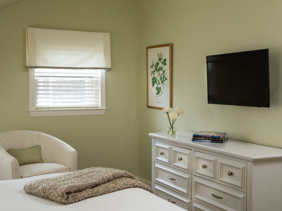 A bedroom with a bed, a chair, a dresser, a television, and a window with blinds.