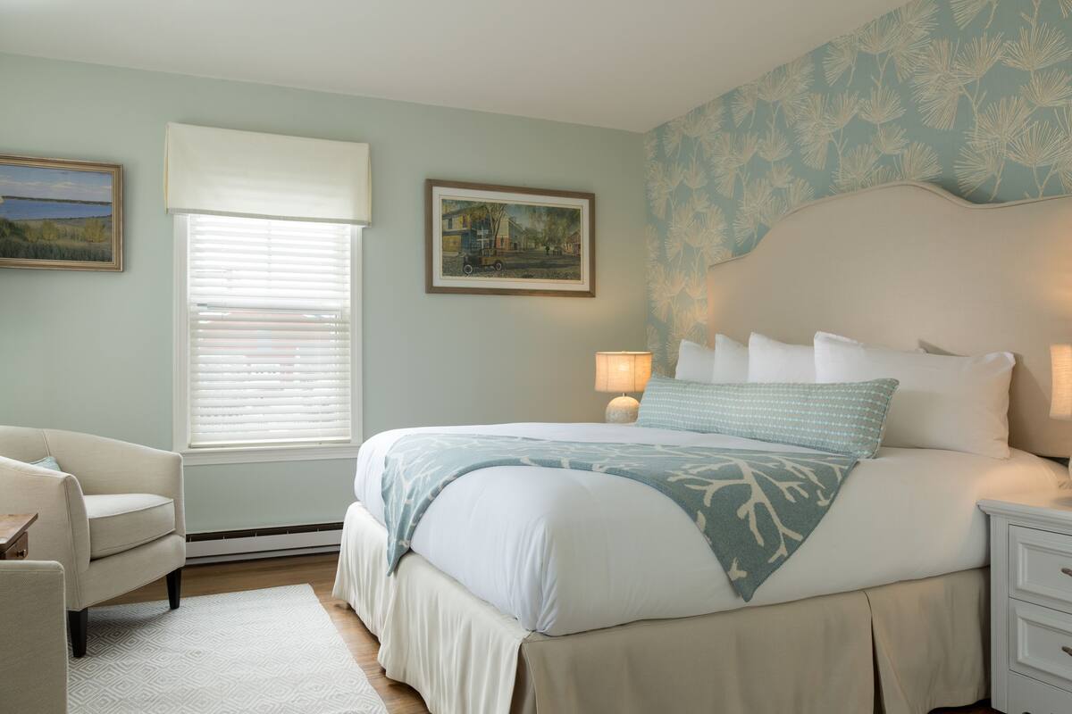 A bedroom with a large bed, two bedside lamps, a chair, and a window with blinds.