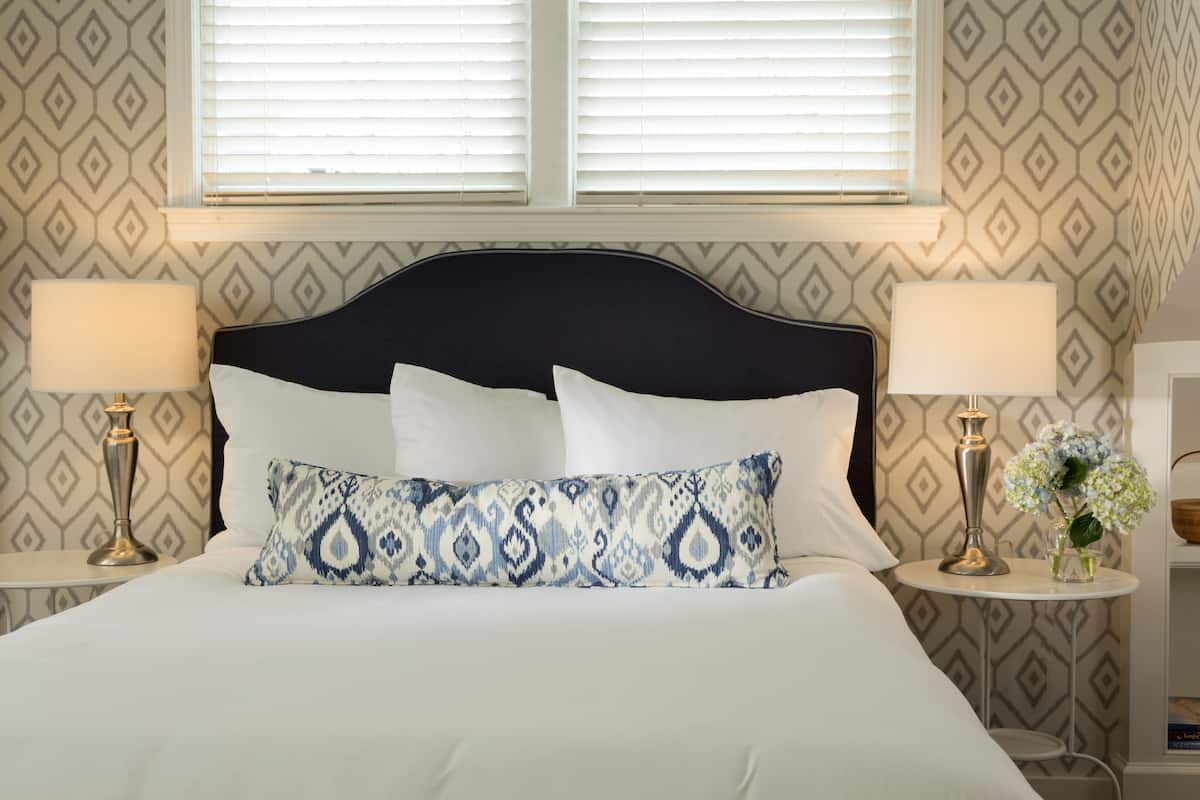 A neatly made bed with white linens, a dark headboard, and two bedside lamps.