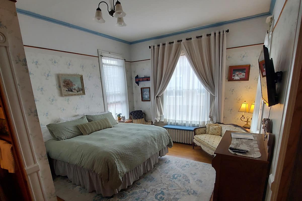 A bedroom with a large bed, a small table, a chair, a radiator, and a television.