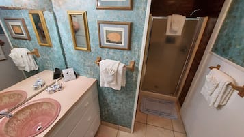 Ein Badezimmer mit einem rosa Waschbecken, mehreren gerahmten Bildern an der Wand und einer Duschkabine.