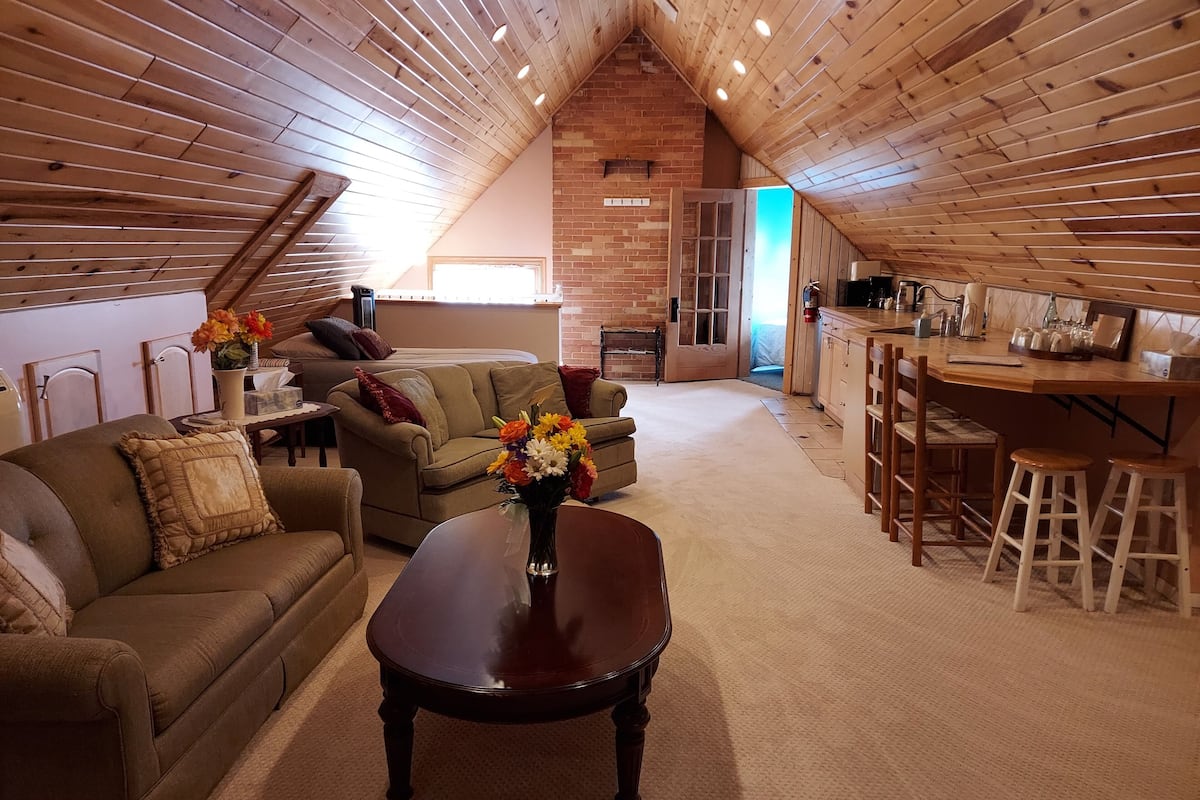A cozy loft-style living space with a wooden ceiling, a dining area with stools, and a kitchen area.