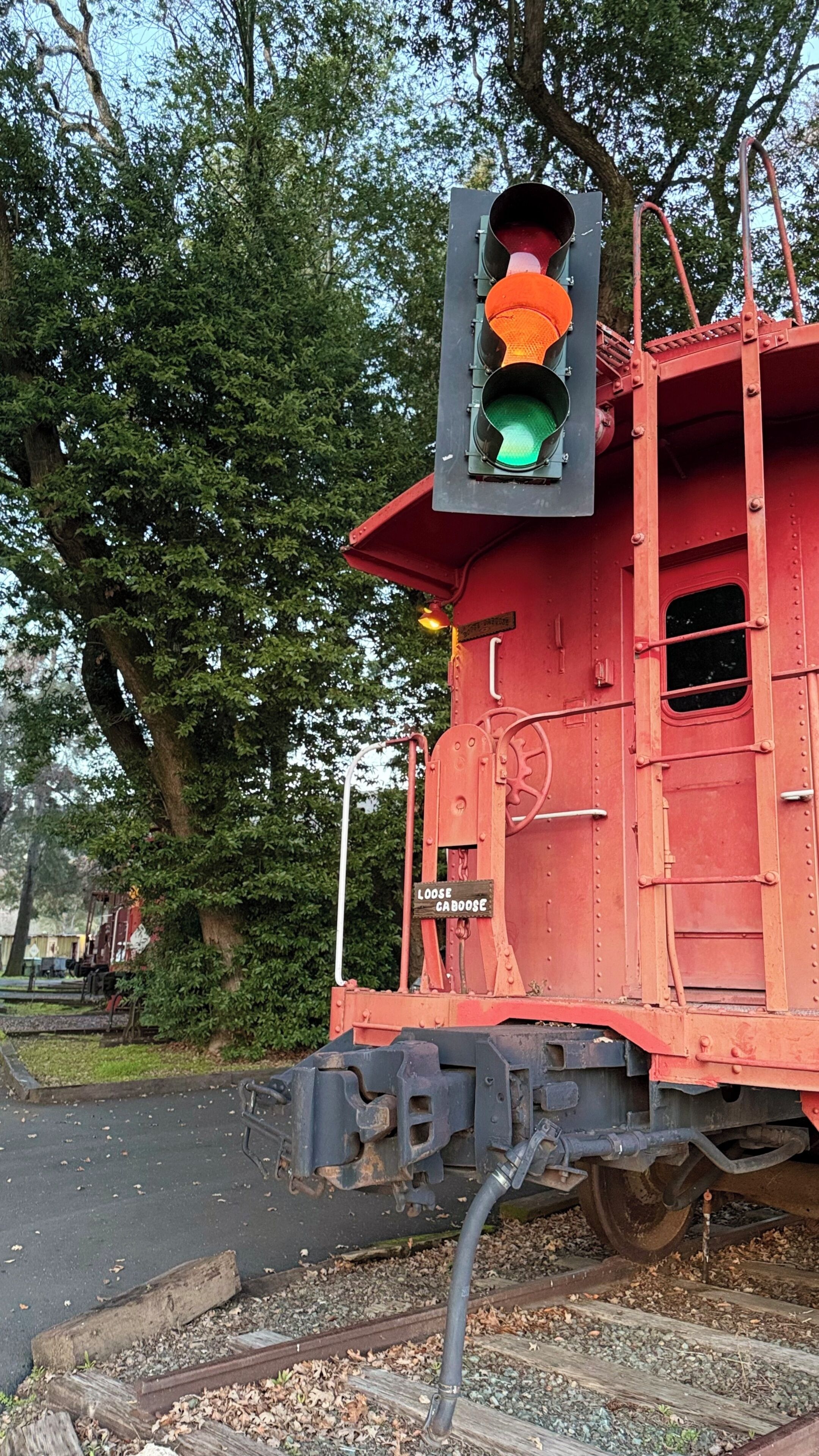 Un carro ferroviario rosso con un semaforo verde montato sopra, un cartello che riporta la scritta 'LOOSE CABOOSE' e un binario con ghiaia.