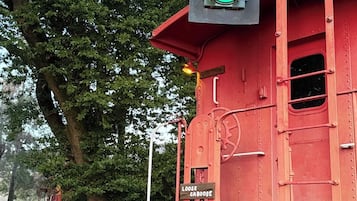Un carro ferroviario rosso con un semaforo verde montato sopra, un cartello che riporta la scritta 'LOOSE CABOOSE' e un binario con ghiaia.