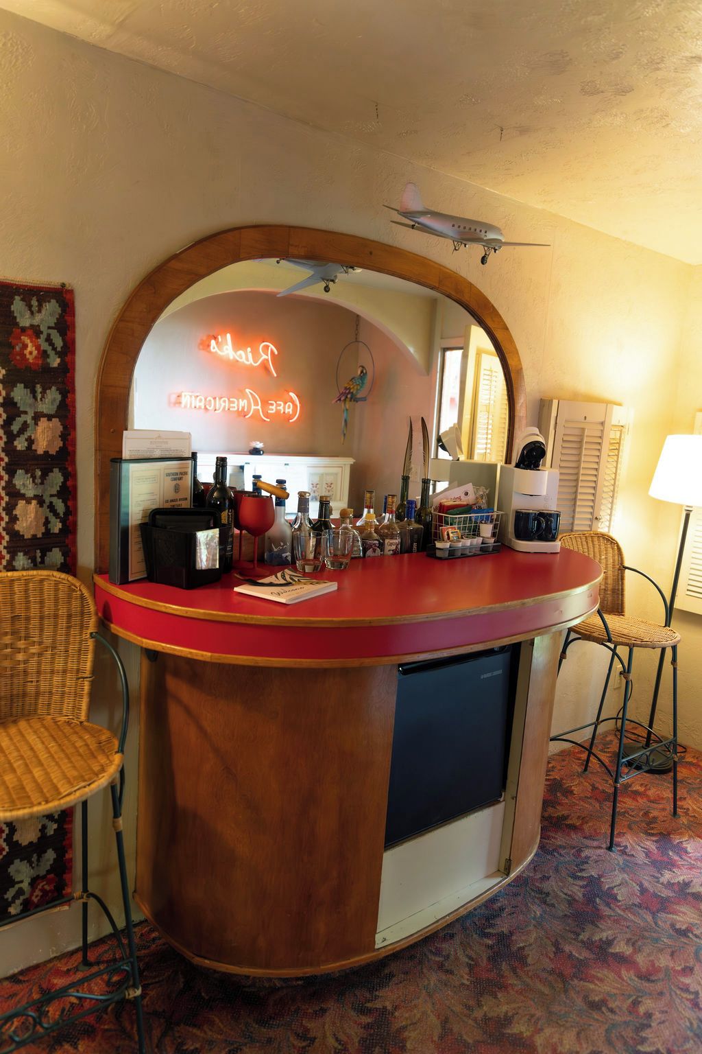 A bar area with a neon sign, a wooden counter, and wicker chairs.