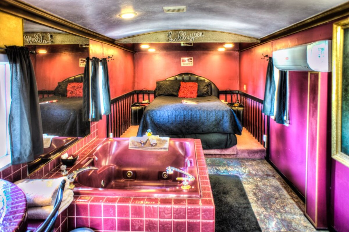 A room with a bed, a large bathtub, and a mirror.