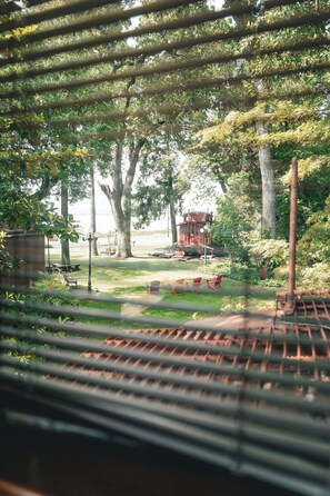 A view through a window with blinds, featuring a garden with a red structure, possibly a gazebo, and a picnic table. - Featherbed Railroad B&B Resort (Nice)