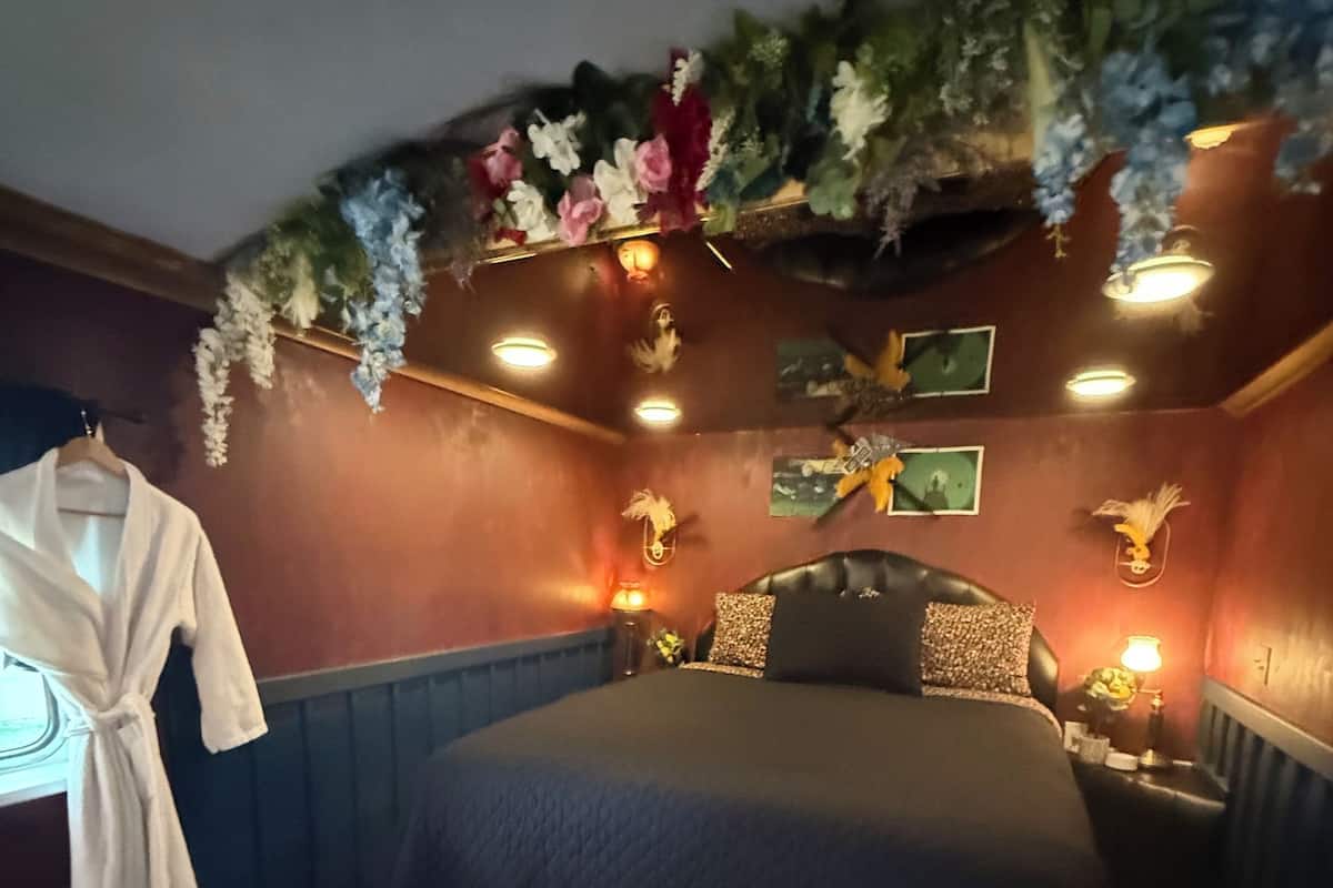Une pièce comprenant un lit, une robe suspendue, une petite table et des lampes fixées au mur.