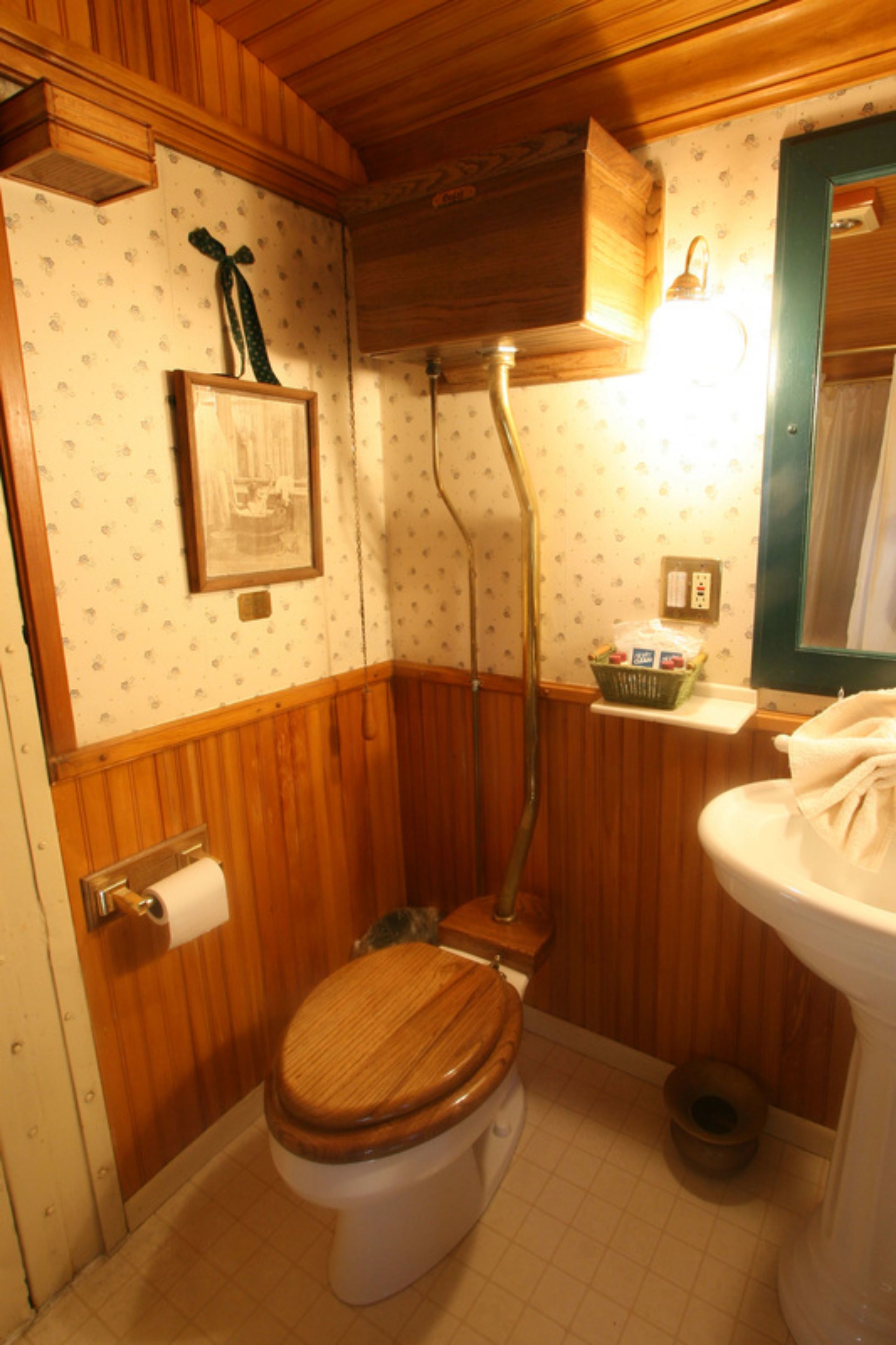 A small, wooden-paneled bathroom with a toilet, a shower, and a sink.