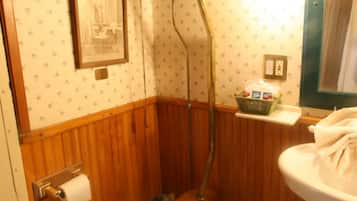 A small, wooden-paneled bathroom with a toilet, a shower, and a sink.