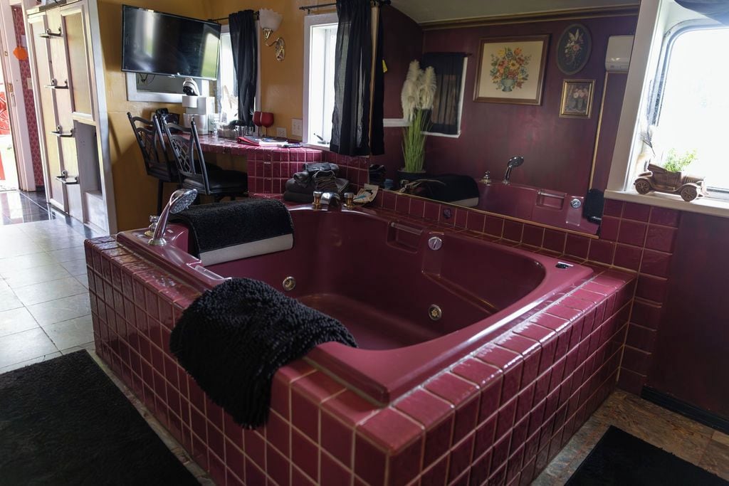 Un baño con una bañera roja grande, un espejo, un lavamanos y un televisor montado en la pared.