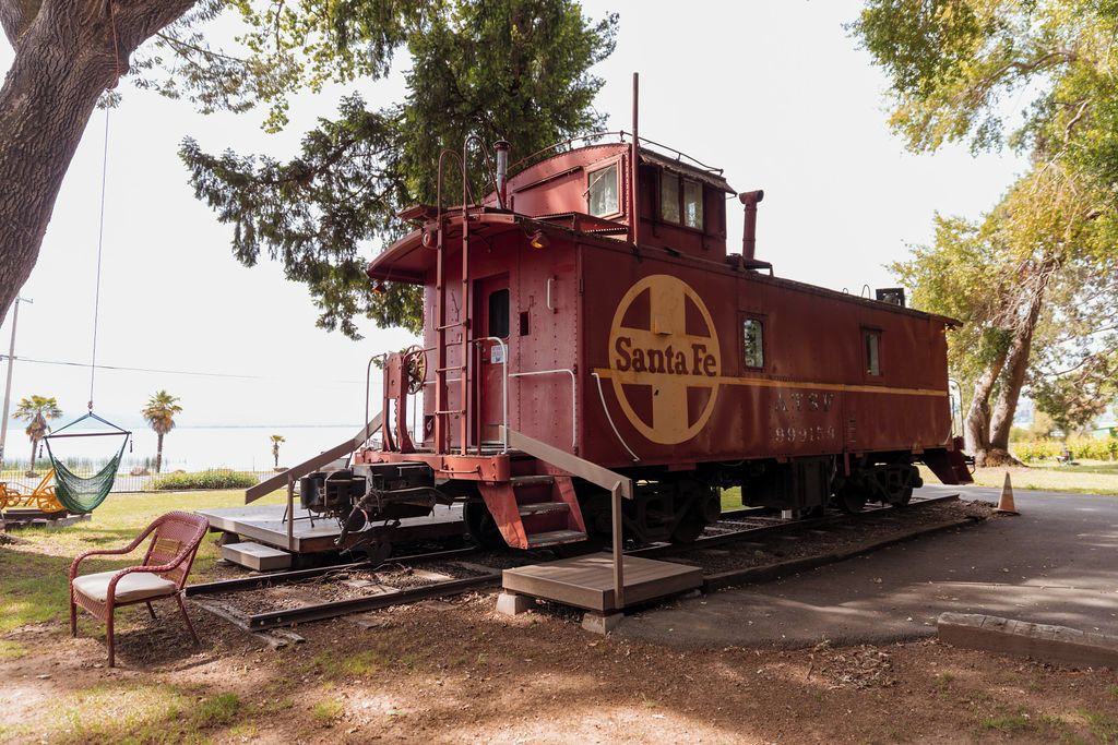 A stationary train caboose with 'Santa Fe' branding, situated on tracks with a chair and a small platform nearby.