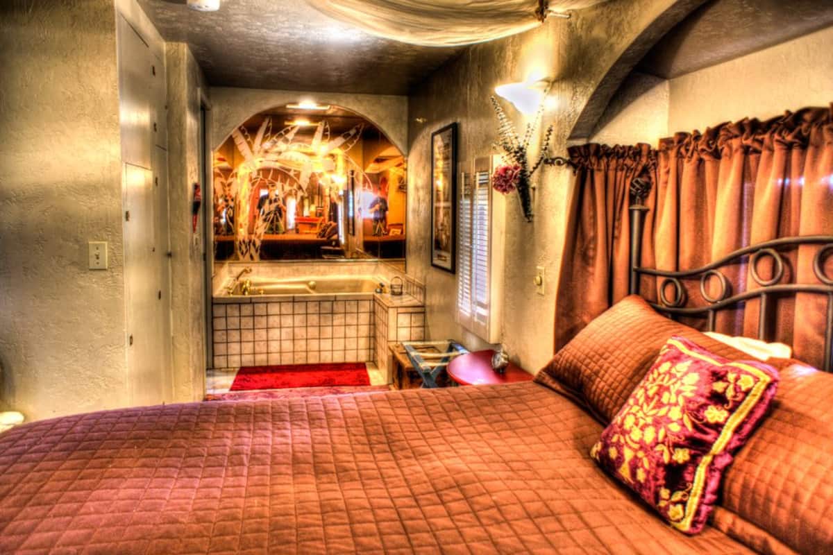 Une chambre avec un grand lit, une salle de bain avec une baignoire et un miroir qui reflète la pièce.