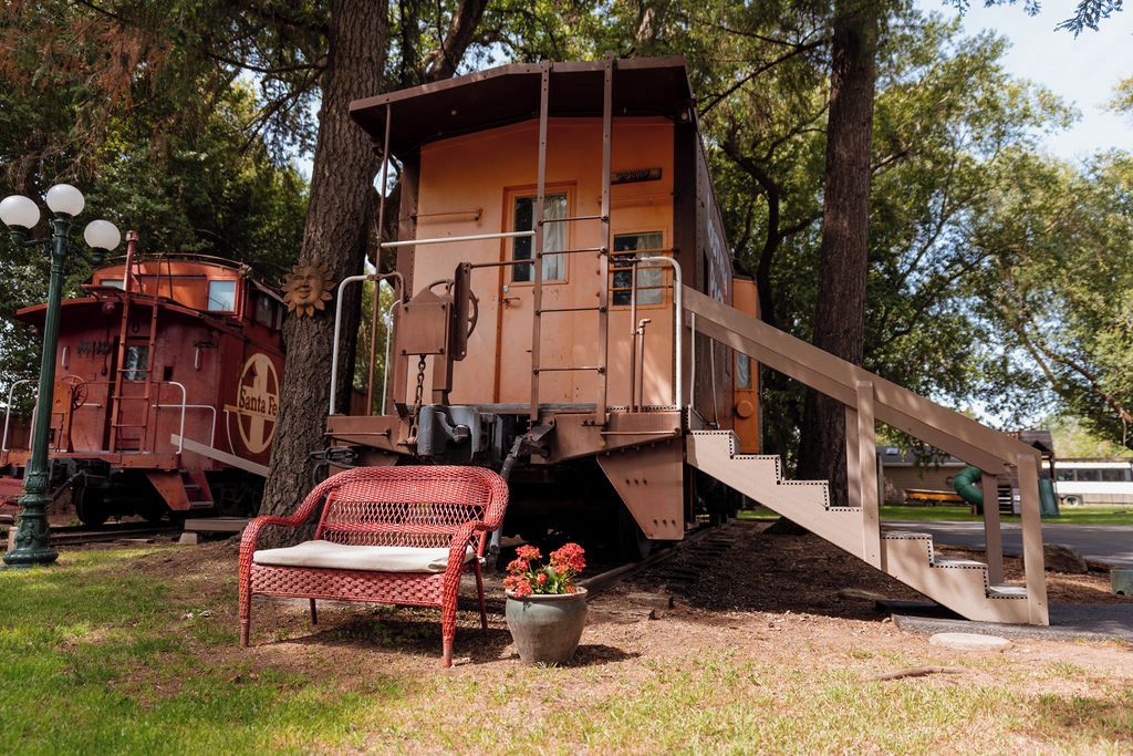 A stationary train car with a staircase leading up to a platform, a bench, and a potted plant with flowers.