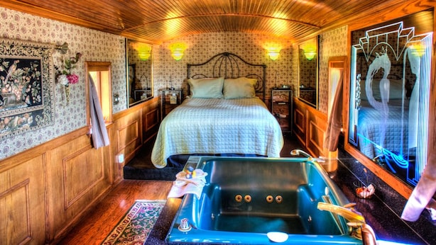 A room with a large bed, a bathtub, wooden paneling, and wall sconces. - Featherbed Railroad B&B Resort (Nice)
