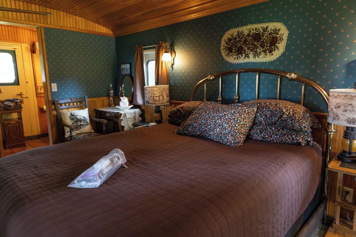 A bedroom with a large bed, a wooden headboard, a nightstand, a lamp, and a window with curtains.