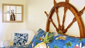 Una cama con cabecera en forma de timón de madera, almohada floral y colcha azul con estampados tropicales.