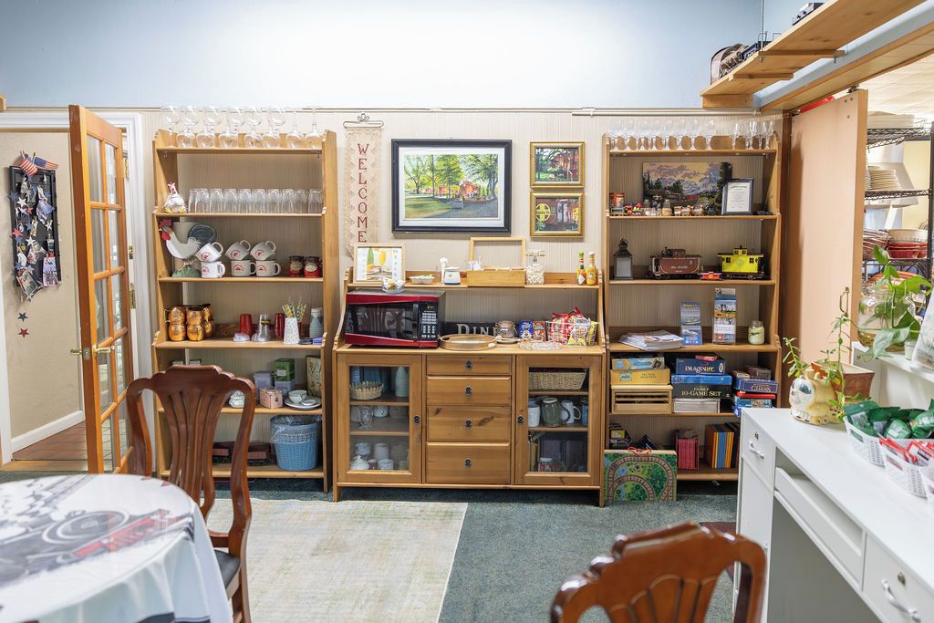 A cozy room with a dining table, chairs, a wooden cabinet with various items, and a bookshelf filled with books and decorative objects.