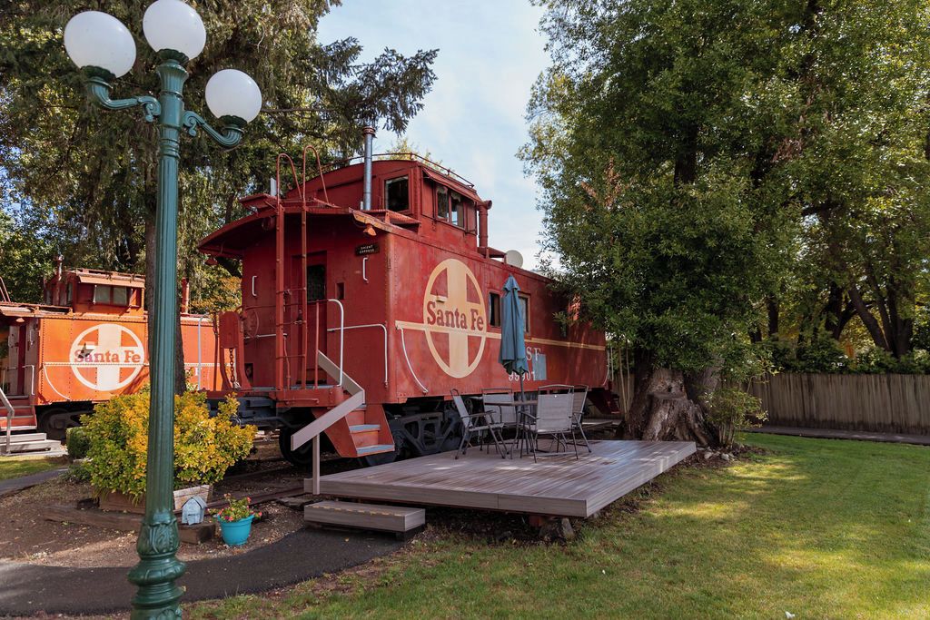 A stationary train caboose with 'Santa Fe' branding, a wooden deck, and outdoor seating.