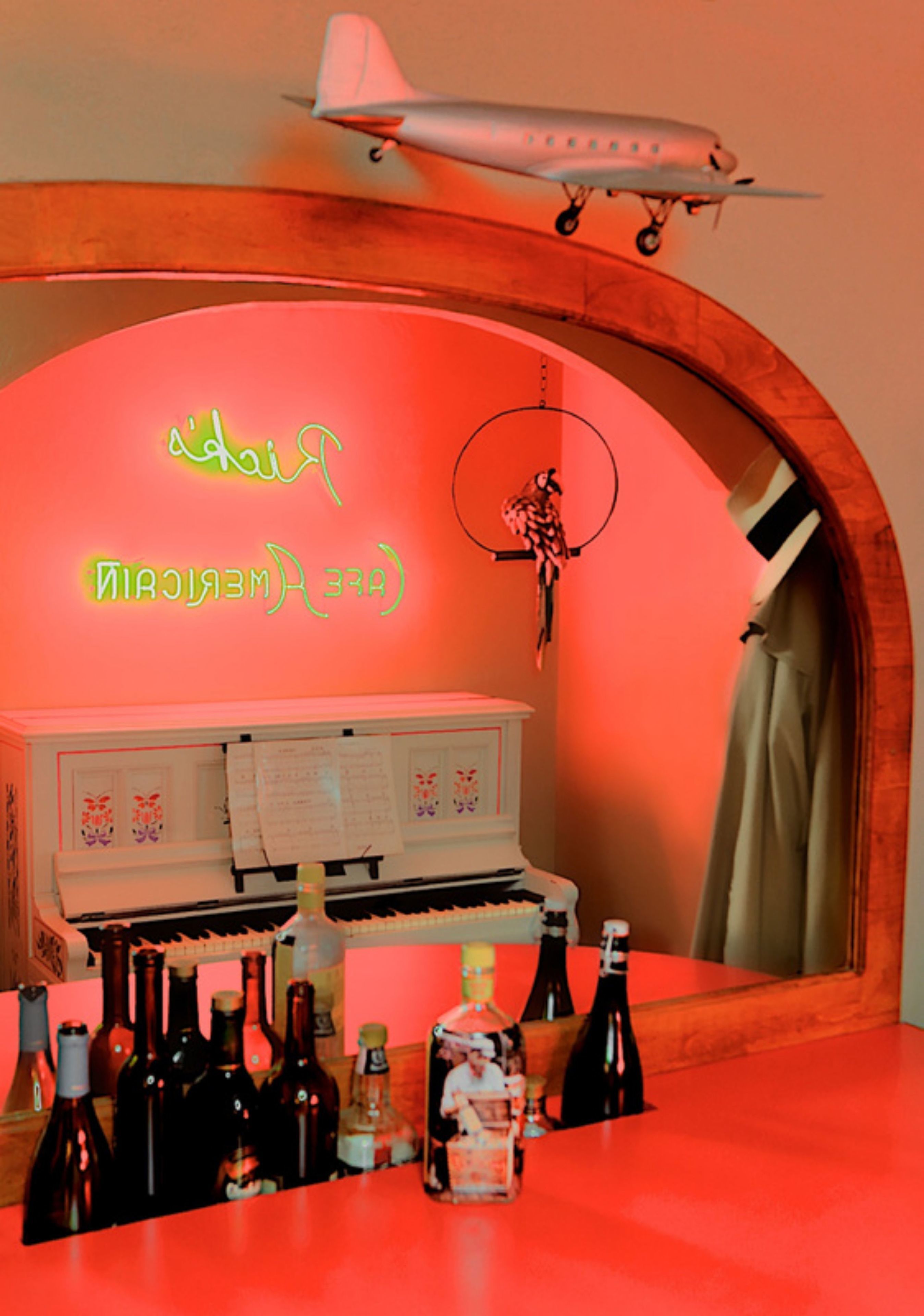 Zona de bar con un letrero de neón, un piano y botellas de alcohol.