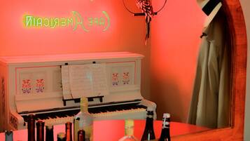 Zona de bar con un letrero de neón, un piano y botellas de alcohol.