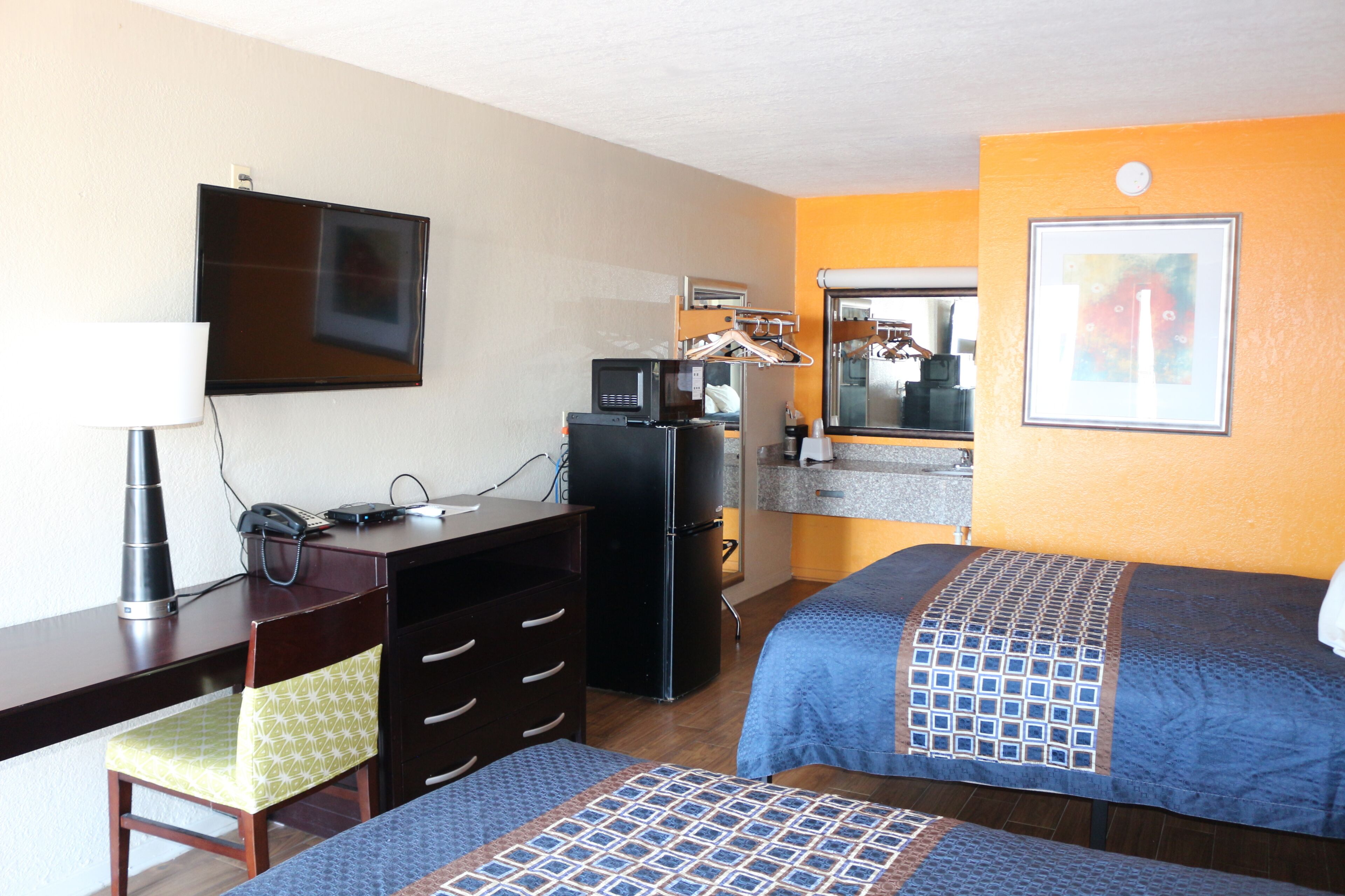 Quarto de hotel com escrivaninha, duas camas, televisão, micro-ondas e frigorífico.