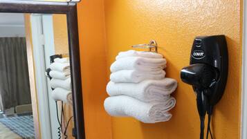 Een badkamer met een granieten wastafel, een spiegel, een haardroger en een handdoekrek met opgevouwen handdoeken.