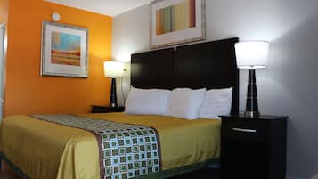 A hotel room with a bed, two bedside tables, a nightstand, a wall clock, and two framed artworks.