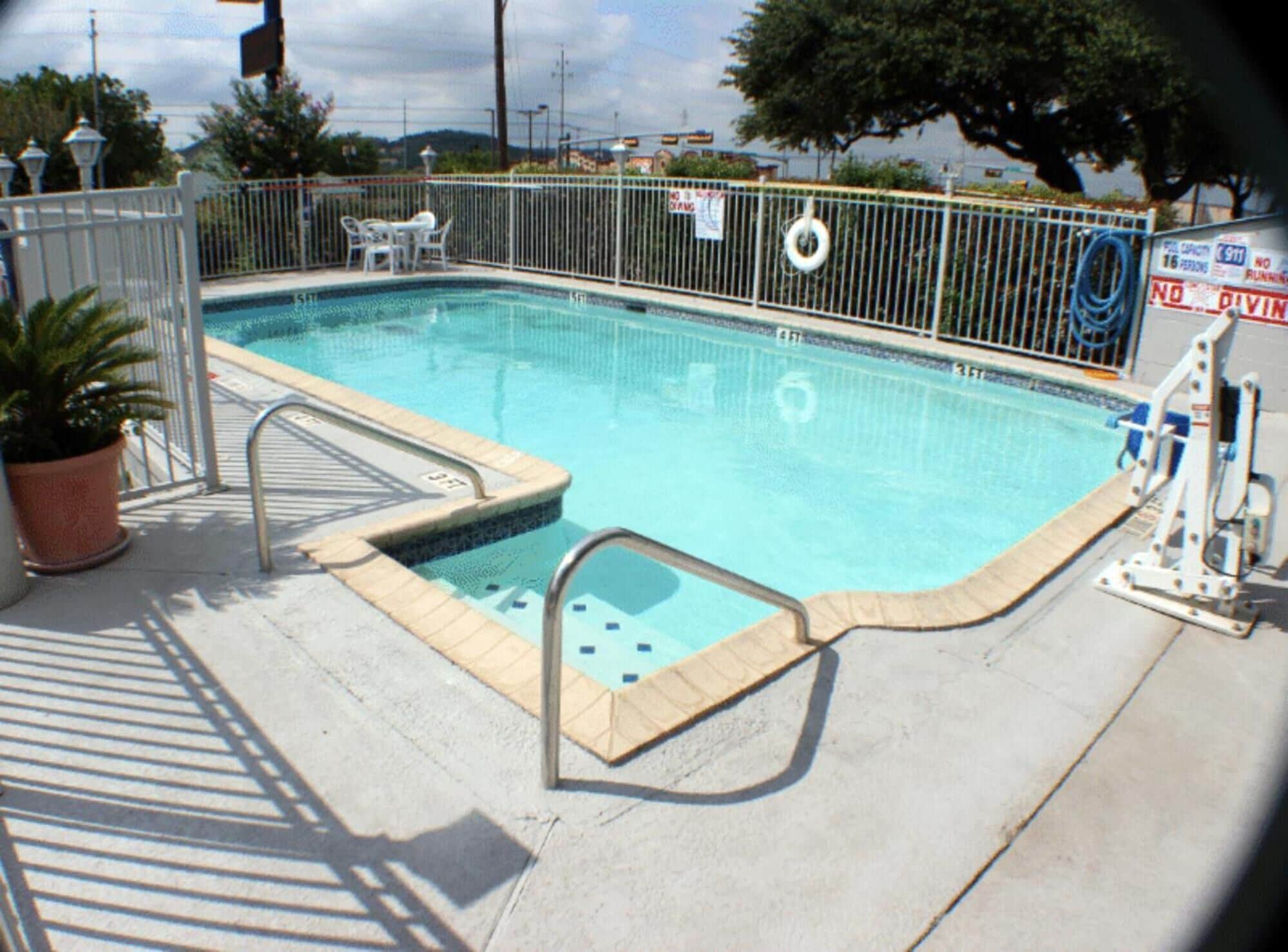 Una piscina rectangular con valla metálica, un flotador salvavidas y una plataforma de salto.