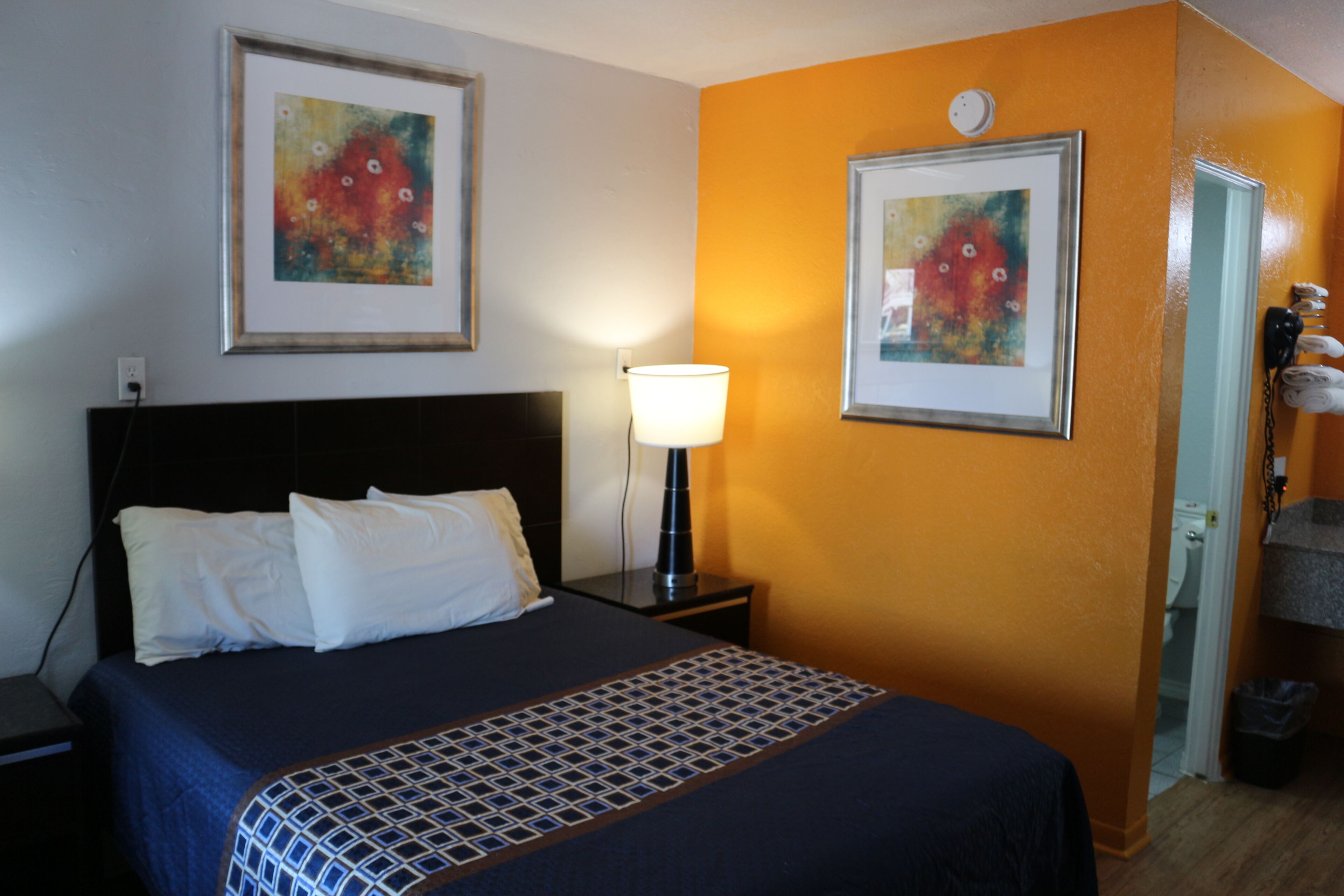 Une chambre d’hôtel avec un lit, une table de chevet, une lampe et deux œuvres d’art encadrées accrochées au mur.