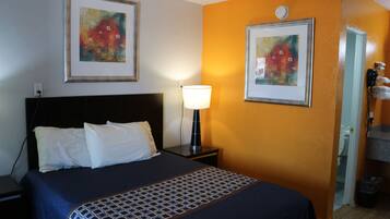 A hotel room with a bed, a nightstand, a lamp, and two framed artworks on the wall.