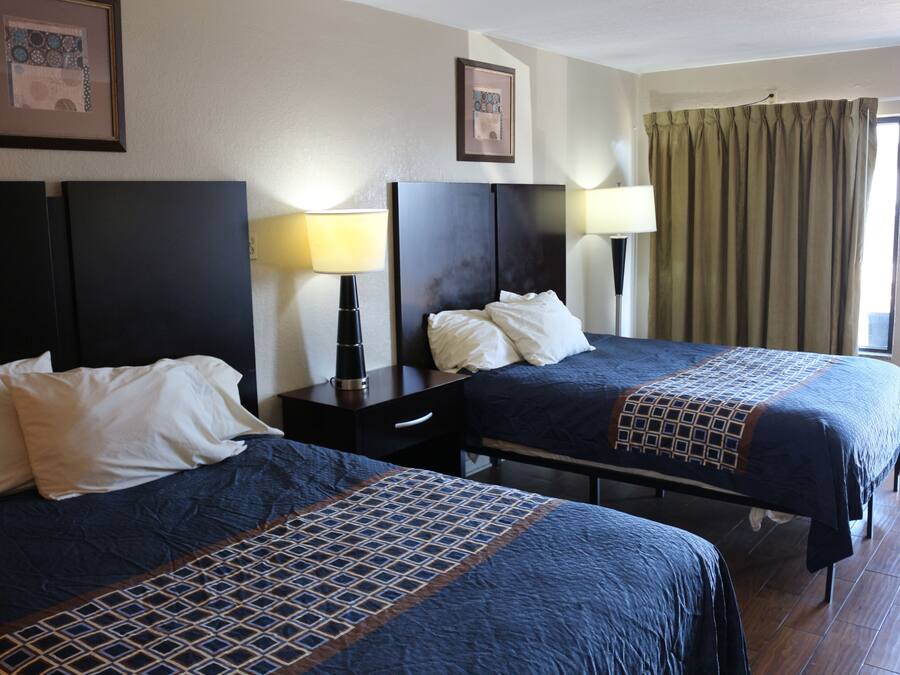 A hotel room with two beds, a nightstand, a lamp, a framed picture on the wall, and a window with curtains.