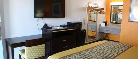 A hotel room with a bed, a desk, a chair, a television, a mirror, and a wardrobe.