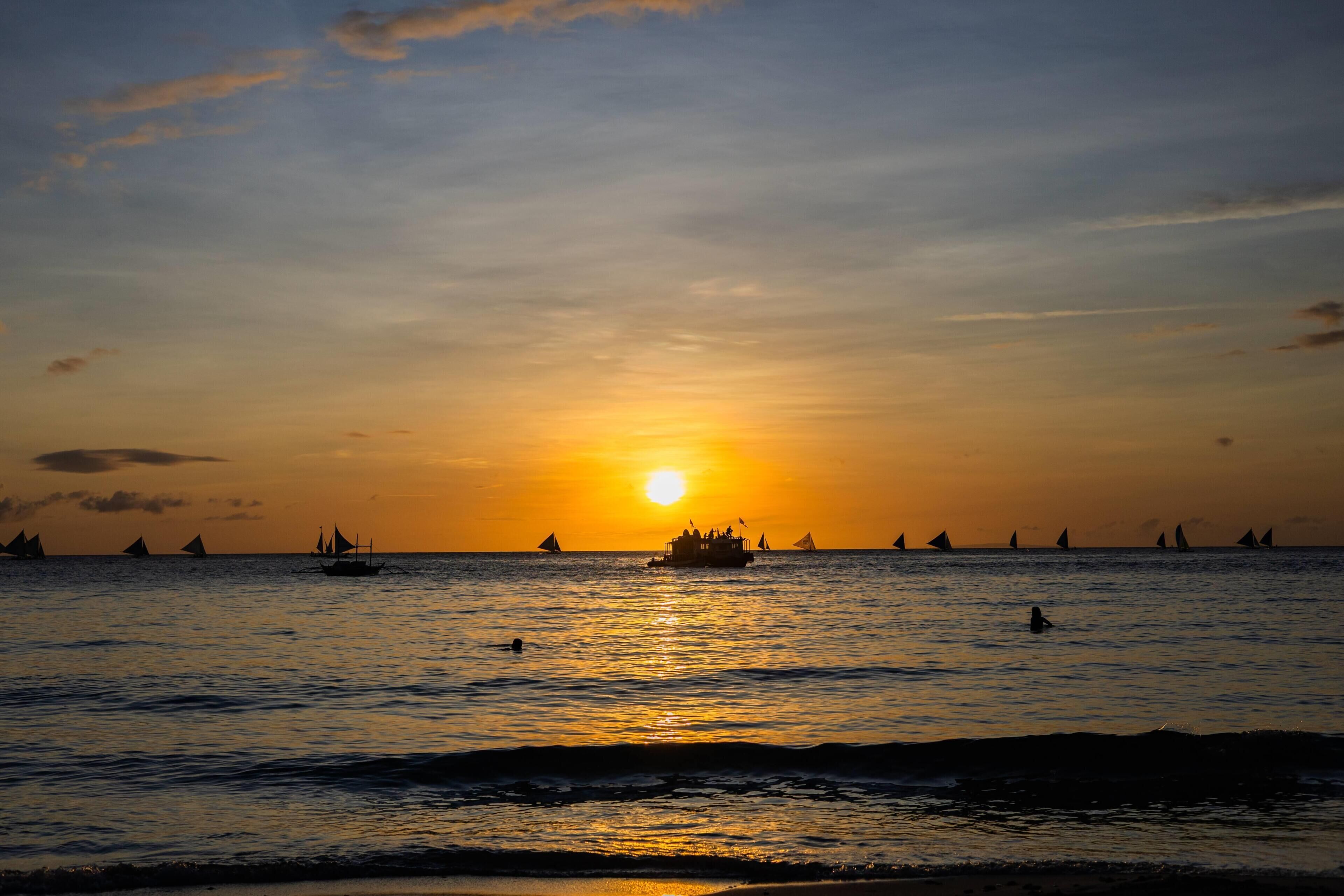 Atardecer sobre un mar tranquilo con barcos y una persona nadando.
