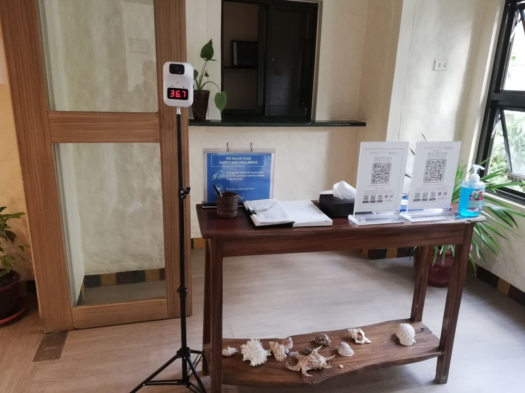A hotel reception desk with a digital thermometer, a blue informational sign, and QR codes for guest services.