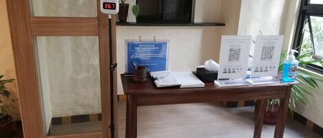 A hotel reception desk with a digital thermometer, a blue informational sign, and QR codes for guest services.