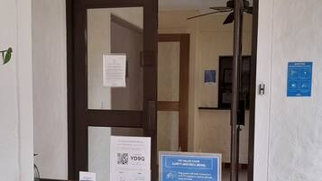 Entrada de hotel con un cartel que indica una acción obligatoria antes de entrar.