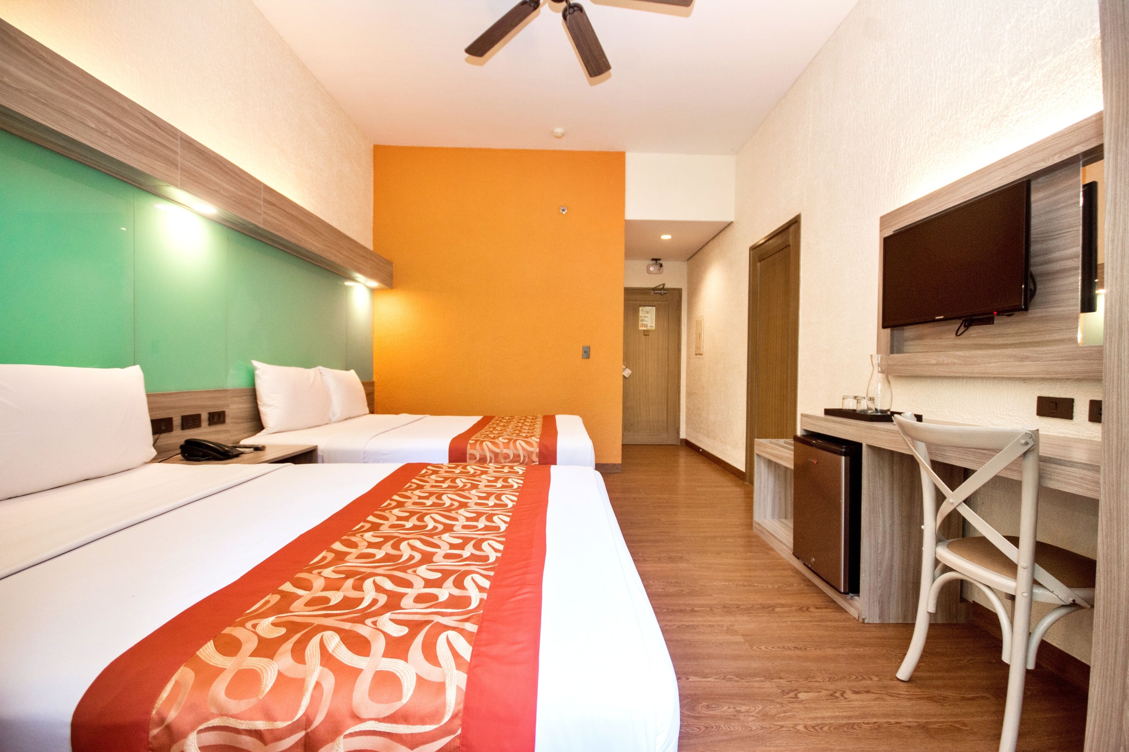 A hotel room with two beds, a TV, a desk, and a bathroom.
