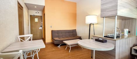 Ein Hotelzimmer mit Holzboden, einer Couch, einem kleinen Tisch, einem runden Tisch, einem Spiegel und einem Deckenventilator.