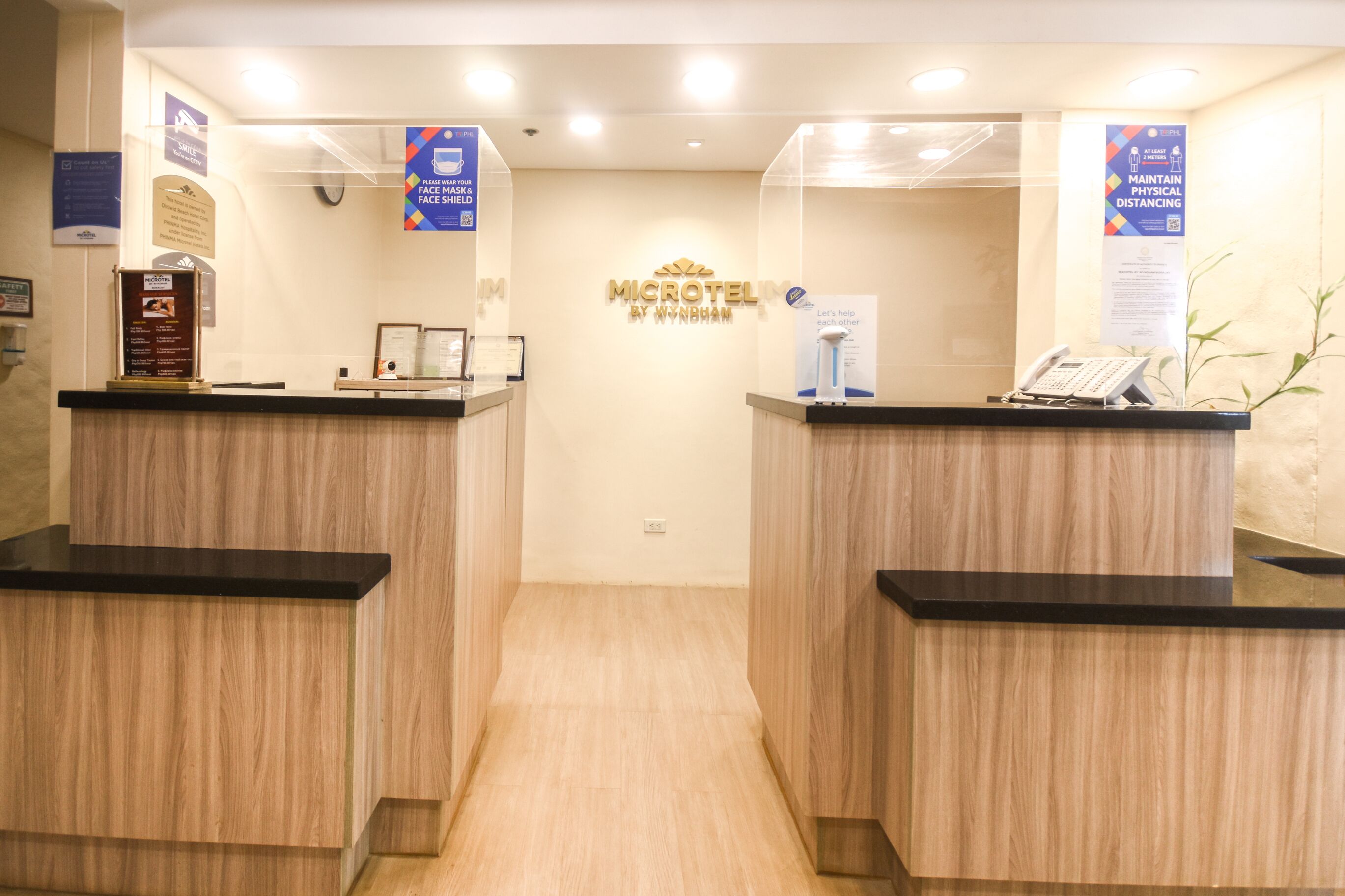 A reception area with two wooden reception desks, a sign for Microtel by Wyndham, and a phone on the right desk.